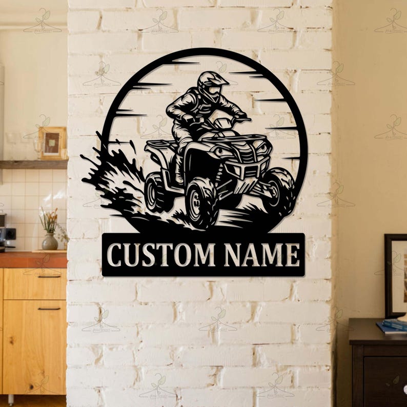 May include: Black metal wall art featuring an ATV rider within a circular frame. The design includes a splash effect and a rectangular plate with the text "CUSTOM NAME". The artwork is mounted on a white brick wall.