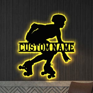 May include: Black silhouette of a roller skater with a helmet and knee pads, illuminated with a warm yellow glow. The text "CUSTOM NAME" is displayed in a horizontal bar. The artwork is mounted on a dark wood-grain background.