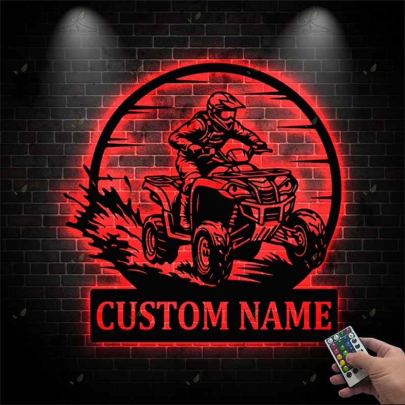 May include: A red, illuminated metal sign featuring a silhouette of a person riding an ATV within a circular frame. The sign includes the text "CUSTOM NAME" in a rectangular panel below the ATV image. The background is a dark brick wall.