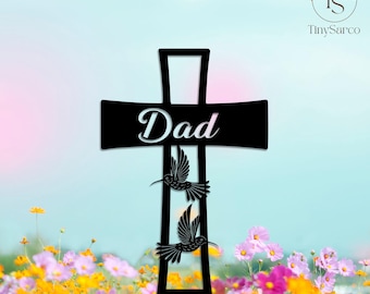 以下が含まれることがあります： 白い筆記体で「Dad」という文字が書かれた黒い金属製の十字架。その下には2羽のハチドリのシルエットが描かれています。十字架は、色とりどりの花と水色の空を背景にしています。