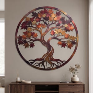 May include: A circular metal wall art piece featuring a tree with intricate roots and branches. The leaves are finished in a gradient of metallic copper, bronze, and deep red tones, enclosed within a matching circular frame with a smooth finish.
