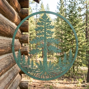 May include: A round, teal metal wall art piece featuring a detailed forest scene. The design includes a central tree with roots, surrounded by smaller trees and foliage, all within a circular frame. The art is mounted on a wooden log cabin wall.