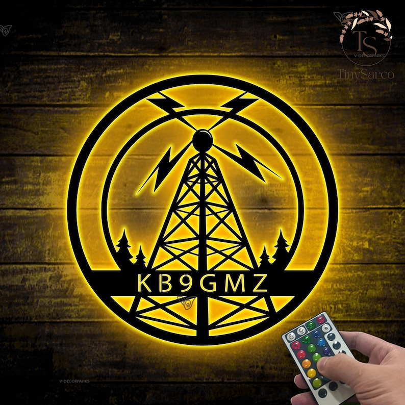 May include: A yellow circle with a black silhouette of a radio tower and lightning bolts inside. The text "KB9GMZ" is below the tower. The circle is on a wood background.