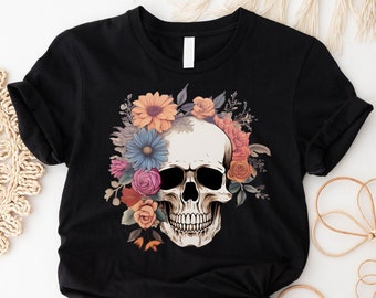 May include: Black t-shirt featuring a detailed skull design adorned with colorful flowers. The floral arrangement includes orange, pink, and blue blooms, creating a striking contrast against the dark fabric. The shirt is a classic crew neck style.