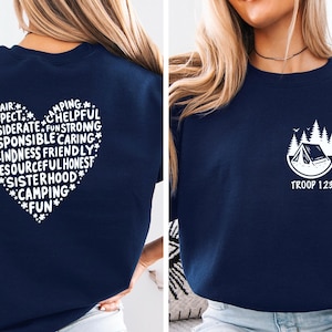 May include: Navy blue sweatshirt with a white heart-shaped design on the back, filled with words like "Respect" and "Kindness." The front features a small white graphic of a tent and trees with the text "Troop 123."