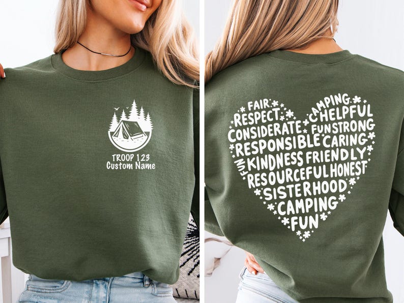 May include: Olive green sweatshirt with a white graphic of a tent and trees, with the text "TROOP 123 Custom Name". The back of the sweatshirt features a heart-shaped design with words like "Camping", "Kindness", and "Fun".