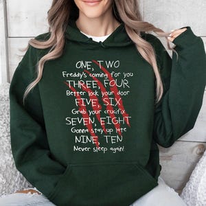 May include: Dark green hoodie with white text and red claw marks. The text reads "ONE, TWO Freddy's coming for you THREE, FOUR Better lock your door FIVE, SIX Grab your crucifix SEVEN, EIGHT Gonna stay up late NINE, TEN Never sleep again!"