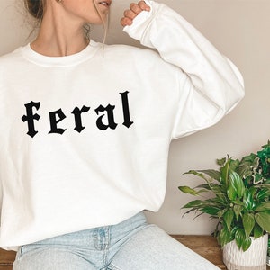 May include: White sweatshirt with the word "feral" printed in black gothic lettering.