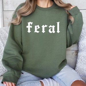 May include: A green sweatshirt with the word "feral" printed in white on the front. The sweatshirt is made of a soft, comfortable material and has a relaxed fit.