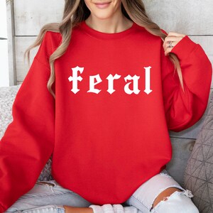 May include: Red sweatshirt with the word "feral" printed in white in a gothic font.
