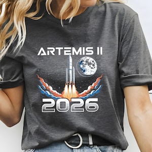 May include: A white ceramic mug with a black handle and the text "But First, Coffee" in a bold, black font. The mug is set against a blurred background, suggesting a cozy setting. The mug appears to be approximately 4 inches tall.