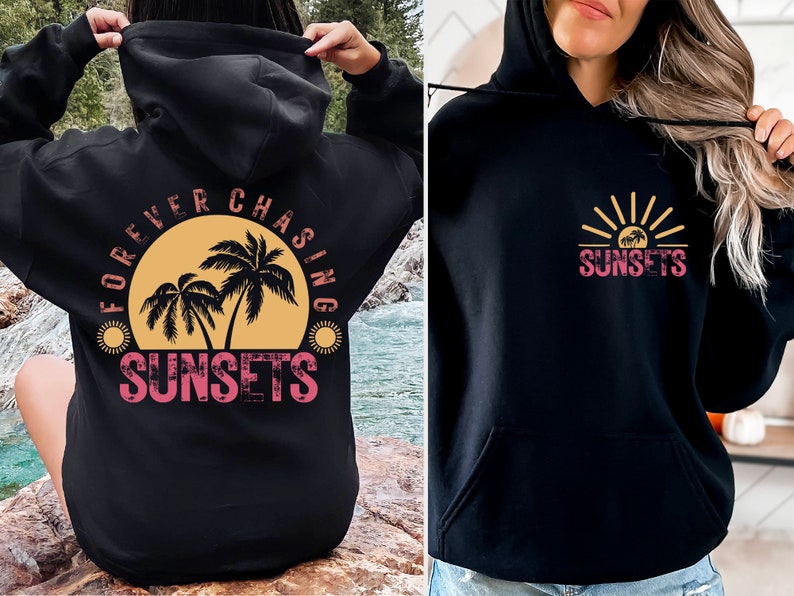 May include: Black hoodie with a graphic print of palm trees and a sunset on the back. The front of the hoodie has a graphic print of a sunset with palm trees and the text "SUNSETS".