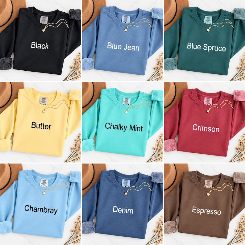 K&ouml;nnte beinhalten: Ein Raster aus neun Rundhals-Sweatshirts in verschiedenen Farben, darunter Schwarz, Blue Jean, Blue Spruce, Butter, Chalky Mint, Crimson, Chambray, Denim und Espresso. Jedes Sweatshirt hat eine kleine goldene Sternhalskette und ein Markenetikett.