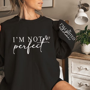 Op de afbeelding: Zwart sweatshirt met de witte tekst "I'M NOT perfect". De mouw heeft de witte tekst "I'M LIMITED edition". Het sweatshirt heeft een casual stijl.