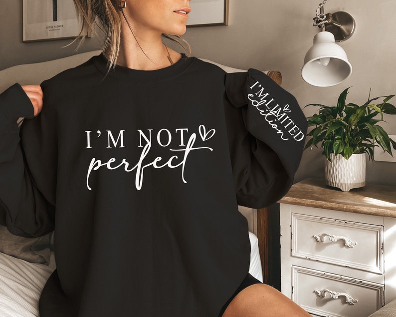 Op de afbeelding: Zwart sweatshirt met de witte tekst "I'M NOT perfect". De mouw heeft de witte tekst "I'M LIMITED edition". Het sweatshirt heeft een casual stijl.