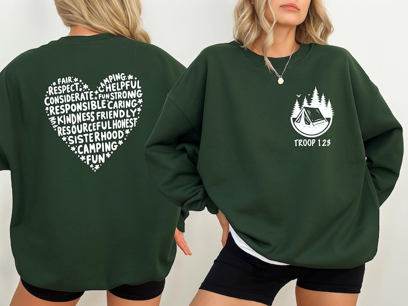 May include: Dark green sweatshirt with white text and graphics. The back features a heart-shaped design with words like "Camping", "Kindness", and "Fun". The front has a camping scene and the text "Troop 123".