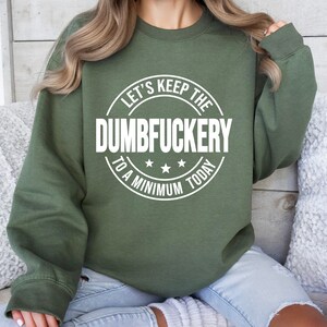 May include: A green sweatshirt with a white circle graphic that says "Let's Keep the Dumbfuckery to a Minimum Today".