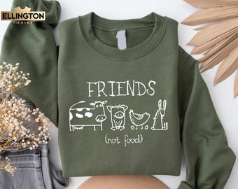 Op de afbeelding: Een groen sweatshirt met de tekst "FRIENDS (not food)" en een witte illustratie van een koe, een varken, een kip en een konijn.