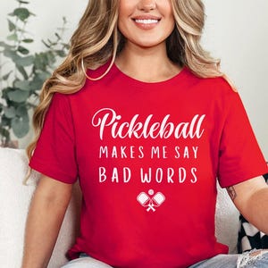 May include: A red t-shirt with white text that reads "Pickleball makes me say bad words" and a white graphic of two pickleball paddles.