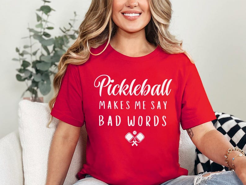 May include: A red t-shirt with white text that reads "Pickleball makes me say bad words" and a white graphic of two pickleball paddles.