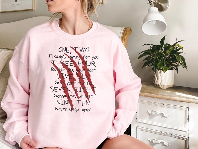 May include: A light pink sweatshirt with the text "ONE, TWO Freddy's coming for you THREE, FOUR Better lock your door FIVE SIX Grab your crucifix SEVEN, EIGHT Gonna stay up late NINE TEN Never sleep again!" and red claw marks.