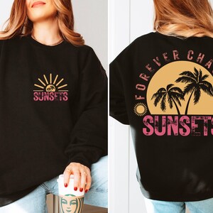 May include: Black sweatshirt with a graphic print of a sunset and palm trees. The front of the sweatshirt says "SUNSETS" and the back says "FOREVER CHASING SUNSETS".