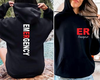 Könnte beinhalten: Schwarze Kapuzenpullover. Einer hat das Wort "EMERGENCY" vertikal in Weiß und Rot auf dem Rücken aufgedruckt. Der andere hat "ER" in Rot und den Namen "Harper" darunter. Beide haben eine Vordertasche und eine Kapuze.