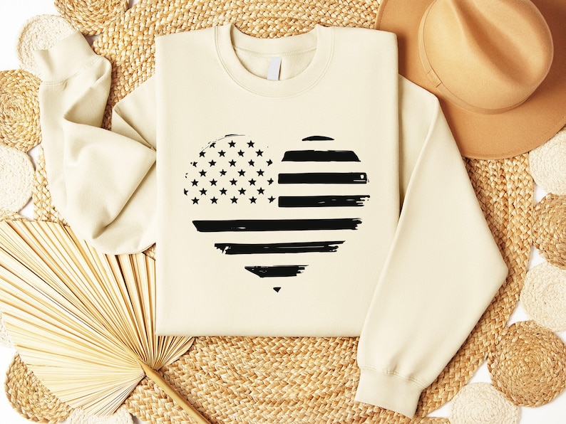 May include: A cream-coloured sweatshirt with a black and white distressed American flag heart design.