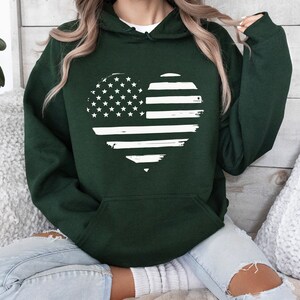 May include: A dark green hooded sweatshirt with a white distressed American flag heart design.
