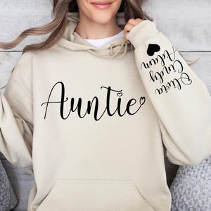 May include: A beige hoodie with the word "Auntie" printed on the front and the words "Olivia,  Curly,  Alan" printed on the sleeve.