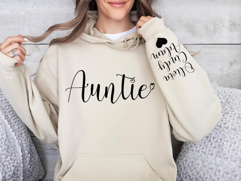 May include: A beige hoodie with the word "Auntie" printed on the front and the words "Olivia,  Curly,  Alan" printed on the sleeve.