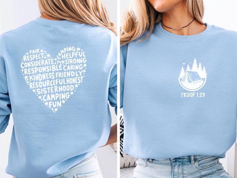 May include: Light blue sweatshirt with a white heart-shaped design on the back, filled with words like 'Respect' and 'Camping'. The front features a white camping scene with the text 'TROOP 123'.