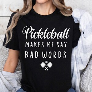 May include: Black t-shirt with white text that reads "Pickleball Makes Me Say Bad Words" and a white graphic of two pickleball paddles and a ball.