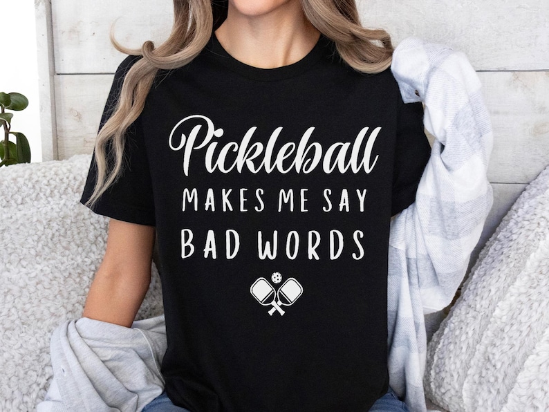 May include: Black t-shirt with white text that reads "Pickleball Makes Me Say Bad Words" and a white graphic of two pickleball paddles and a ball.