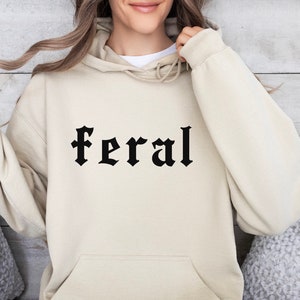 May include: A cream colored hoodie with a black gothic font print that says "feral".