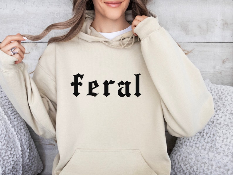 May include: A cream colored hoodie with a black gothic font print that says "feral".