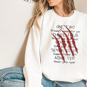 May include: White sweatshirt with the text "ONE, TWO Freddy's coming for you THREE, FOUR Better lock your door FIVE SIX Grab your crucifix SEVEN, EIGHT Gonna stay up late NINE TEN Never sleep again!" and red claw marks.