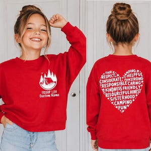 May include: Red sweatshirt with a white camping graphic and text "TROOP 123 Custom Name" on the front. The back features a heart-shaped design with words like "FAIR", "RESPECT", and "CAMPING".