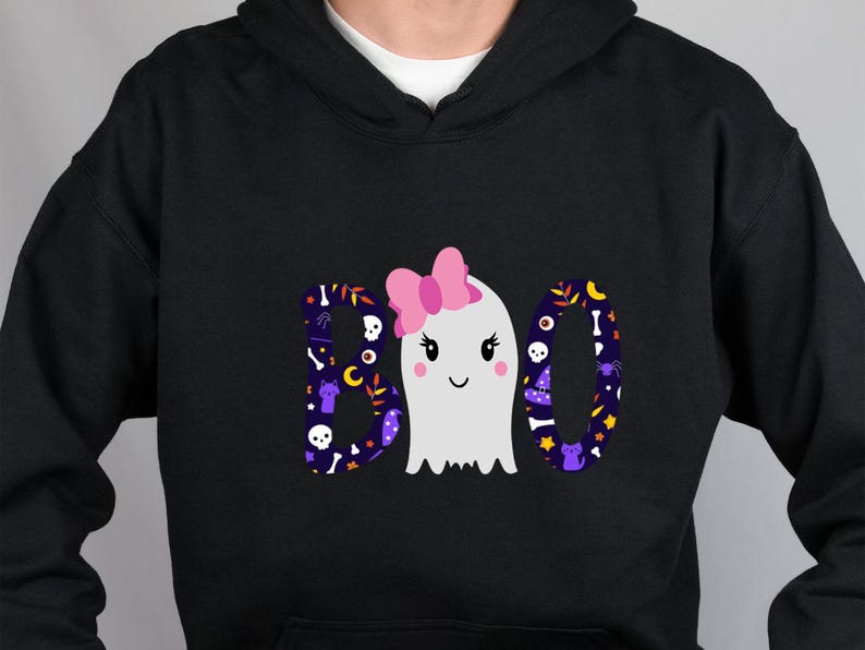 May include: A black hooded sweatshirt featuring a graphic print of the word BOO. The letters B and O are filled with a dark purple pattern of skulls, bones, and cats. A white ghost with a pink bow replaces the letter O in the center.