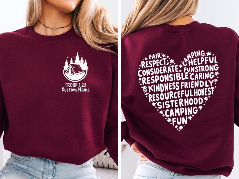 May include: Burgundy sweatshirt with a white camping-themed graphic on the front and a heart-shaped design on the back. The front graphic includes a tent, trees, and the text "TROOP 123 Custom Name." The back features words like "Respect," "Kindness," and "Camping."