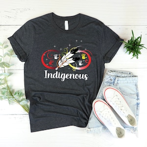 May include: A dark grey t-shirt with an infinity symbol design featuring a feather and handprints in red, yellow, orange, and black. The text "Indigenous" is printed below the symbol.