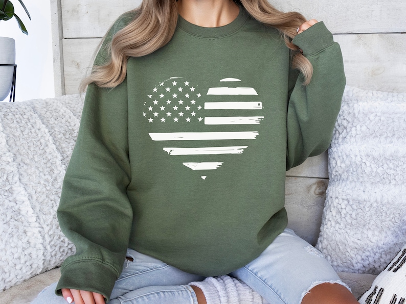 May include: A green sweatshirt with a white distressed American flag heart design.