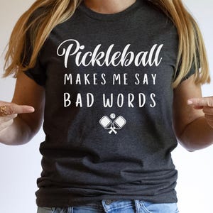 May include: A dark grey t-shirt with white text that reads "Pickleball Makes Me Say Bad Words" and a graphic of two pickleball paddles and a ball.