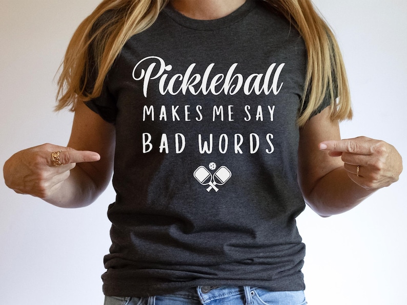 May include: A dark grey t-shirt with white text that reads "Pickleball Makes Me Say Bad Words" and a graphic of two pickleball paddles and a ball.