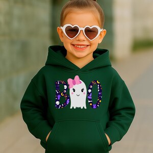 May include: A dark green hooded sweatshirt featuring a graphic print of the word BOO, where the letter O is replaced by a white ghost wearing a pink bow. The letters B and O are filled with a pattern of skulls, moons, and stars.