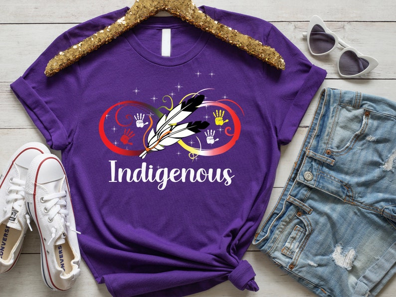 May include: Purple t-shirt with an infinity symbol design featuring a feather and handprints in red, yellow, and blue. The word "Indigenous" is printed below the symbol.