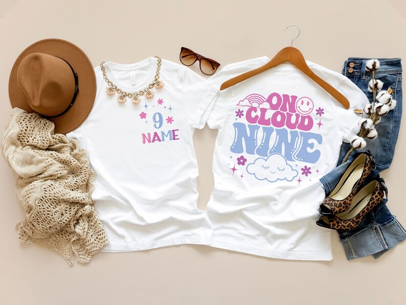 May include: Two white t-shirts with colorful graphics. One shirt has the number 9 and the word "NAME" in a pink and blue gradient. The other shirt says "ON CLOUD NINE" with a rainbow, smiley face, and cloud graphic.