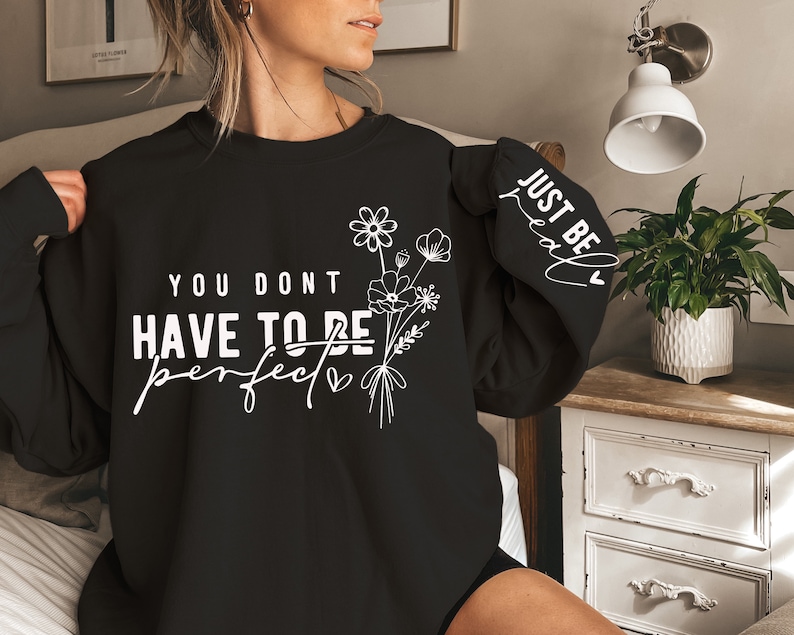 May include: Black sweatshirt with the text "You don't have to be perfect" and a floral design. The right sleeve has the text "Just be real" with a heart.