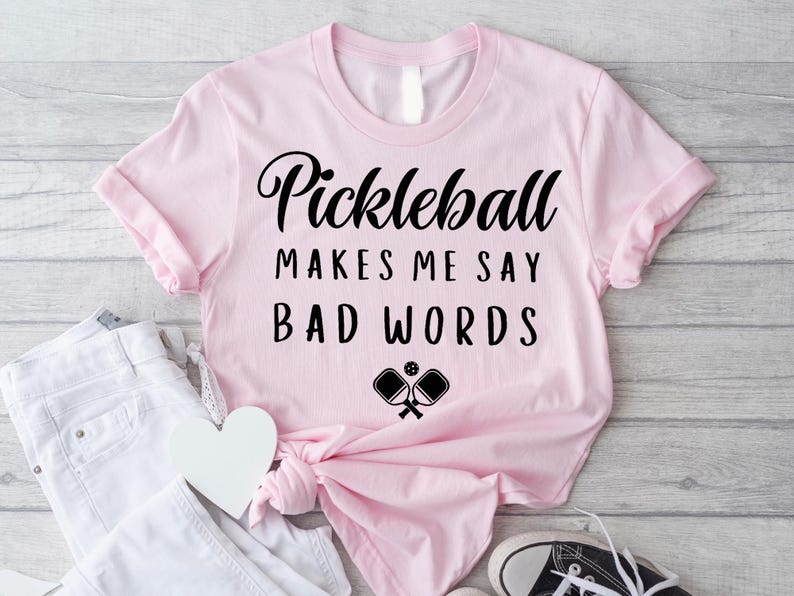 May include: Pink t-shirt with the text "Pickleball makes me say bad words" and a black and white illustration of two pickleball paddles.