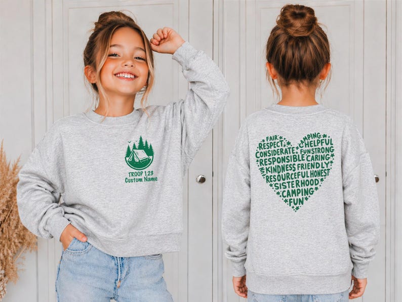 May include: A light gray sweatshirt with a green camping-themed graphic on the front and a heart-shaped design on the back. The front graphic includes a tent, trees, and the text "TROOP 128 Custom Name." The back features words like "Fair," "Respect," and "Camping."